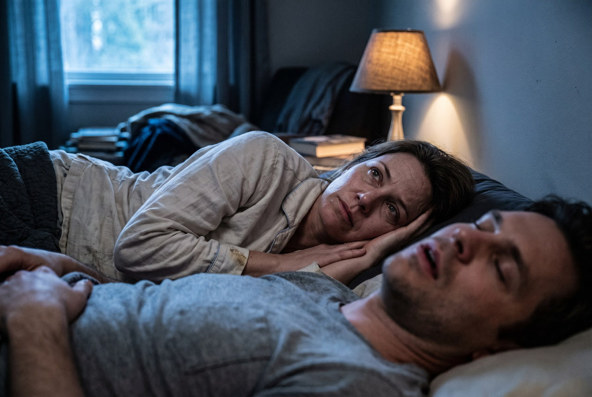 A couple in bed at night. One is asleep, the other is awake.